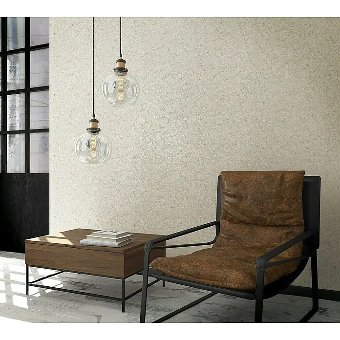 Marburg Vintage Deluxe Vliestapete Craquelée-Risse - Beige, Grafisch, 10,05 x 0,53 m - Elegantes Wohnzimmer mit stilvollem Sessel, Holzbeistelltisch mit Büchern und zwei modernen Pendelleuchten für eine gemütliche Atmosphäre.