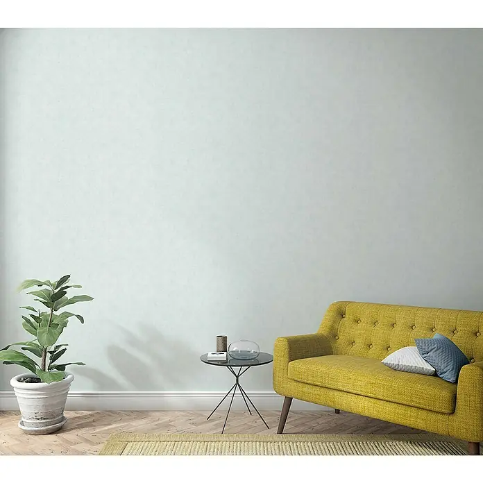 Marburg Shades Vliestapete - Weißgrau, Uni, 10,05 x 0,53 m - Einladendes Interieur mit einem gelben Sofa, einem Beistelltisch mit Dekoration und einer Zimmerpflanze, die eine gemütliche Atmosphäre schaffen.