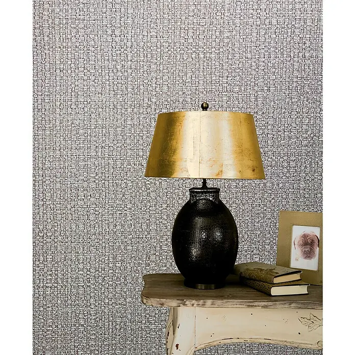 Marburg Vintage Deluxe Vliestapete Retro - Greige, Uni, 10,05 x 0,53 m - Nahaufnahme einer stilvollen Nachttischlampe mit goldfarbenem Schirm, Büchern und einem Bilderrahmen auf einem verzierten Beistelltisch.