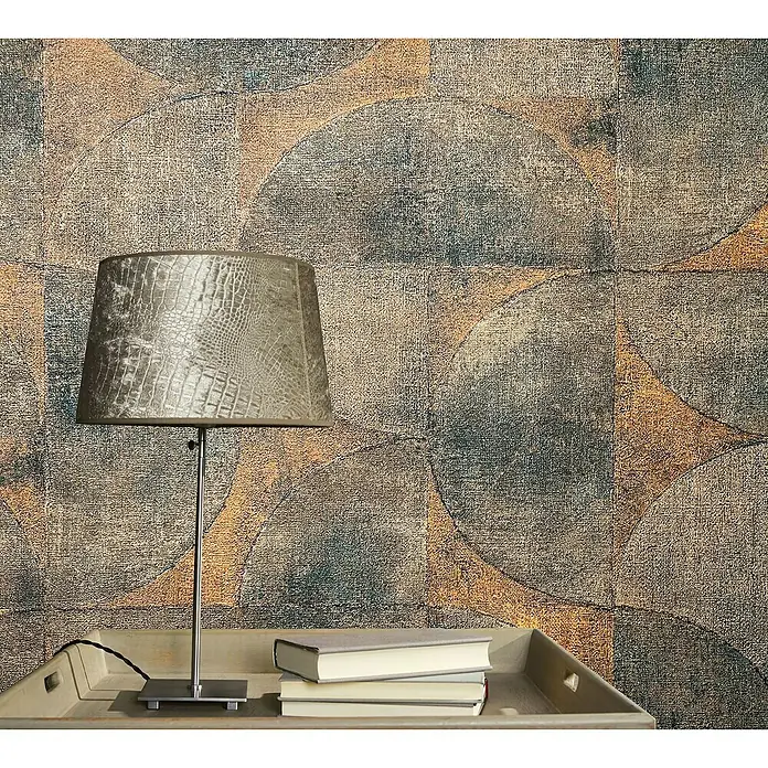 Marburg Vintage Deluxe Vliestapete - Kupfer-Anthrazit, Grafisch, 10,05 x 0,53 m - Nahaufnahme einer modernen Nachttischlampe mit Reptilienmuster-Schirm und Büchern auf einem Tablett vor einer gemusterten Wand.