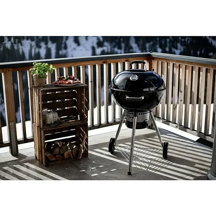 Kingstone Kugelgrill Bullet 57 - Durchmesser Grillfläche: 57 cm, Schwarz - Kugelgrill und Holzkiste auf einer Terrasse mit Blick auf schneebedeckte Berge. Perfekt für ein Barbecue im Freien mit stilvollem Ambiente.