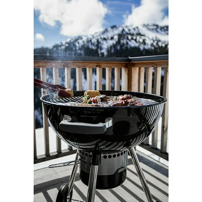 Kingstone Kugelgrill Bullet 57 - Durchmesser Grillfläche: 57 cm, Schwarz - Grill mit Essen auf einem Balkon mit Bergblick. Der runde Holzkohlegrill steht bereit für ein gemütliches Barbecue mit Bergpanorama.