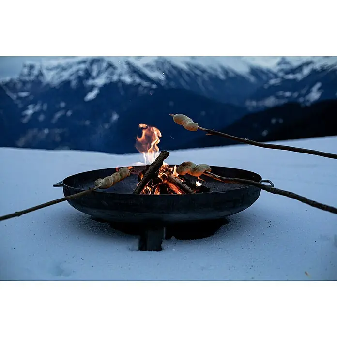 Feuerschale - Durchmesser: 80 cm, Eisen - Stockbrot wird über einem Lagerfeuer in einer Feuerschale im Schnee geröstet, im Hintergrund verschneite Berge.