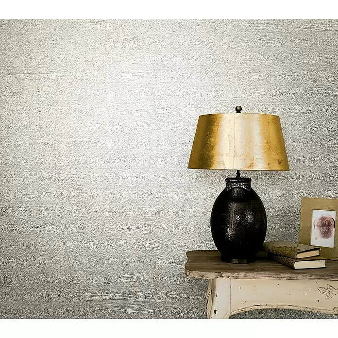 Marburg Vintage Deluxe Vliestapete - Greige, Uni, 10,05 x 0,53 m - Schwarz-goldene Tischlampe auf einem patinierten Beistelltisch mit Büchern.