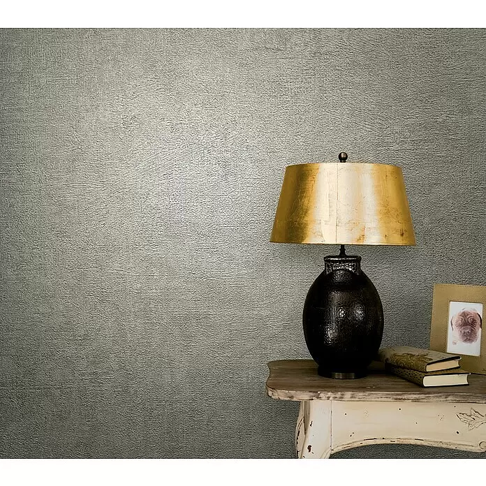 Marburg Vintage Deluxe Vliestapete - Beige, Uni, 10,05 x 0,53 m - Texturierte graue Tapete an einer Wand, die eine stilvolle Kulisse für Lampe und Tisch bietet.