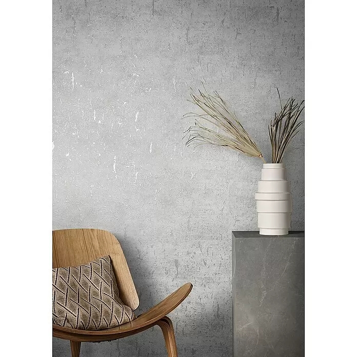 Marburg Natural Opulence Vliestapete - Weiß II, Betonoptik, 10,05 x 0,7 m - Abgenutzte graue Betonoptik-Wand in modernem Interieur mit Holzstuhl und Vase mit getrockneten Palmblättern.