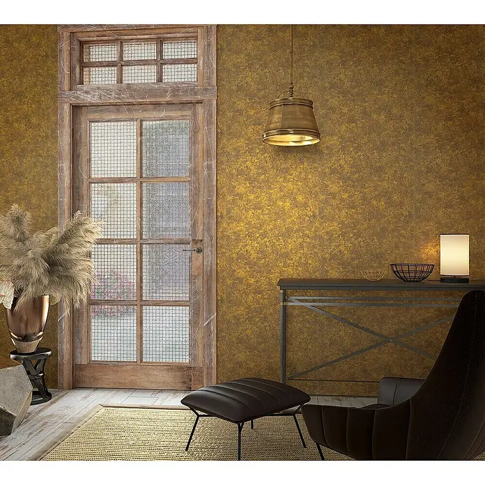 Marburg Natural Opulence Vliestapete Struktur I - Gold, Betonoptik, 10,05 x 0,7 m - Einrichtung mit einem Lampenschirm in Messing-Optik, einem Tisch mit Dekoration und einem bequemen Sessel. Das goldfarbene Wanddekor schafft eine warme Atmosphäre.