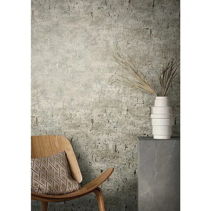Marburg Natural Opulence Vliestapete - Beige, Betonoptik, 10,05 x 0,7 m - Detailaufnahme eines Raumes mit strukturierten Wandtapeten, einem Sessel mit Kissen und einer minimalistischen Vase mit Trockenblumen.