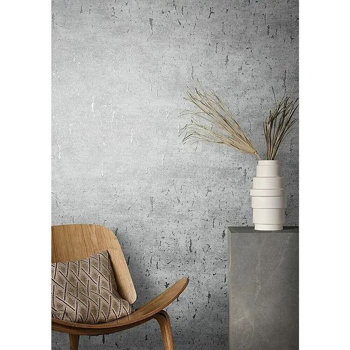 Marburg Natural Opulence Vliestapete - Weiß-Grau, Betonoptik, 10,05 x 0,7 m - Ein stilvolles Interieur mit einem modernen Holzstuhl und einer dekorativen Vase vor einer strukturierten Wand.