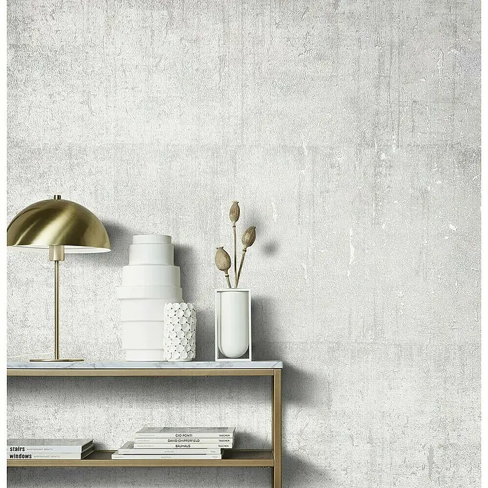 Marburg Natural Opulence Vliestapete - Weiß I, Betonoptik, 10,05 x 0,7 m - Nahaufnahme eines stilvollen Tisches mit Dekorationen wie einer Lampe, Vasen und Büchern, die ein elegantes und modernes Ambiente schaffen.