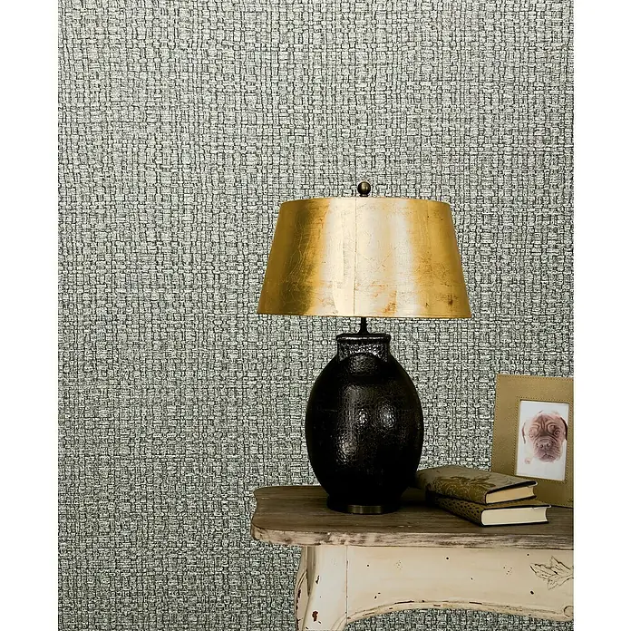 Marburg Vintage Deluxe Vliestapete Retro - Beige, Uni, 10,05 x 0,53 m - Nahaufnahme einer stilvollen schwarzen Tischlampe mit goldenem Schirm auf einem dekorierten Beistelltisch vor einer strukturierten Wand.