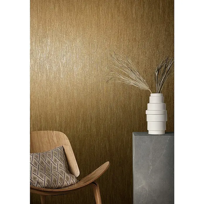 Marburg Natural Opulence Vliestapete - Braun, Streifen, 10,05 x 0,7 m - Elegantes Interieur mit Fokus auf goldfarbener Tapete, akzentuiert durch einen stilvollen Stuhl und eine moderne Vase.