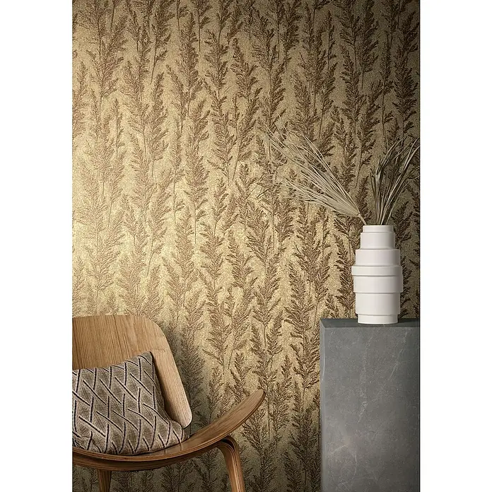 Marburg Natural Opulence Vliestapete Weiche Gräser - Gold, Floral, 10,05 x 0,7 m - Nahaufnahme einer Wandtapete mit floralem Muster, einem Holzsessel und einer dekorativen Vase auf einem grauen Sockel.