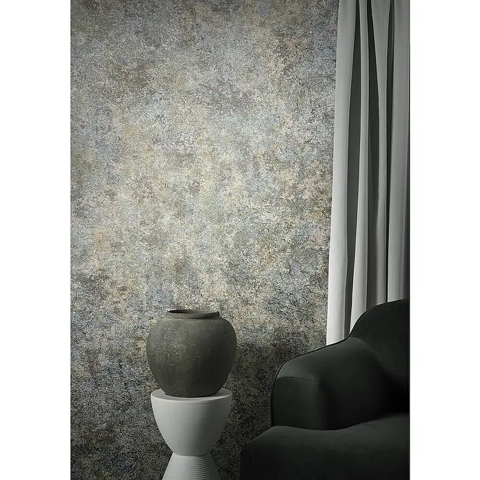 Marburg Natural Opulence Vliestapete Struktur I - Grau-Grün, Betonoptik, 10,05 x 0,7 m - Dekorative Keramikvase auf einem Beistelltisch neben einem Sessel, vor einer strukturierten Wand und Vorhängen.