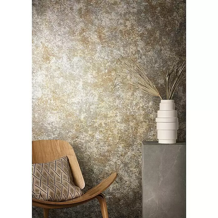 Marburg Natural Opulence Vliestapete Struktur I - Braun, Betonoptik, 10,05 x 0,7 m - Texturierte Wand in warmen Gold- und Weißtönen, bildet eine stilvolle Kulisse für einen modernen Holzstuhl und eine Vase.