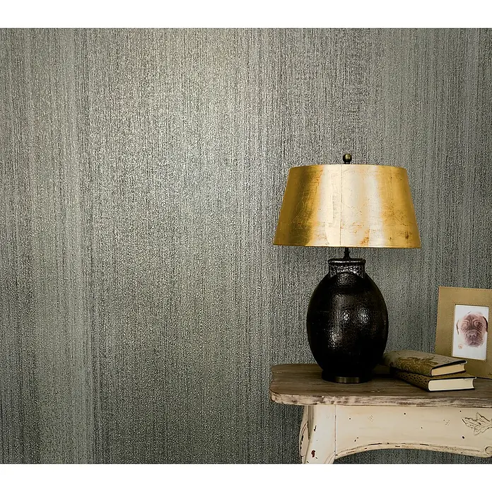 Marburg Vintage Deluxe Vliestapete - Grau-Gold, Streifen, 10,05 x 0,53 m - Elegante Studioaufnahme einer goldenen Lampe auf einem Tisch, vor einer strukturierten Wand, für dekorative Zwecke.