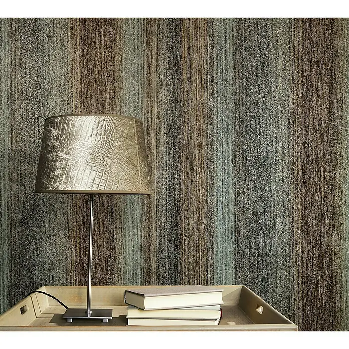 Marburg Vintage Deluxe Vliestapete - Gold-Anthrazit, Streifen, 10,05 x 0,53 m - Nahaufnahme einer Tischlampe mit Schirm im Kroko-Design, platziert auf einem Nachttisch mit Büchern vor einer strukturierten Wand.