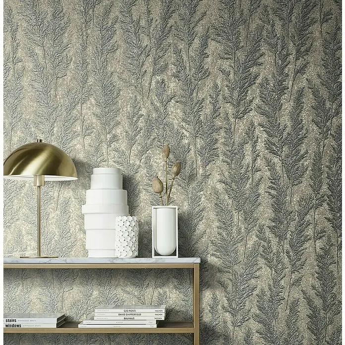 Marburg Natural Opulence Vliestapete Weiche Gräser - Platin, Floral, 10,05 x 0,7 m - Nahaufnahme einer dekorierten Konsole mit einer goldenen Lampe und Designer-Büchern vor einer blättrigen Tapete.