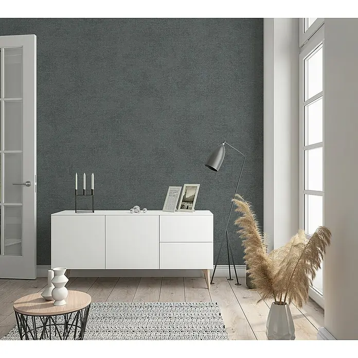 Marburg Shades Vliestapete - Anthrazit, Uni, 10,05 x 0,53 m - Elegantes Sideboard in Weiß mit Dekorationen, Lampe und einem Tisch mit Vasen auf einem hellen Holzboden vor einer dunklen Wand.