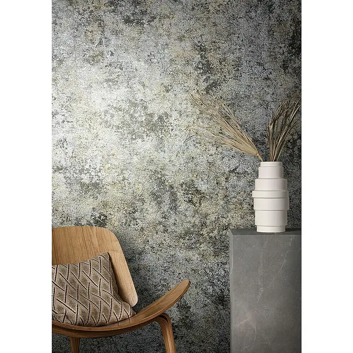 Marburg Natural Opulence Vliestapete Struktur I - Silber, Betonoptik, 10,05 x 0,7 m - Elegantes Interieur mit einem Stuhl mit Kissen und einer weißen Vase auf einem Sockel vor einer strukturierten Wand.