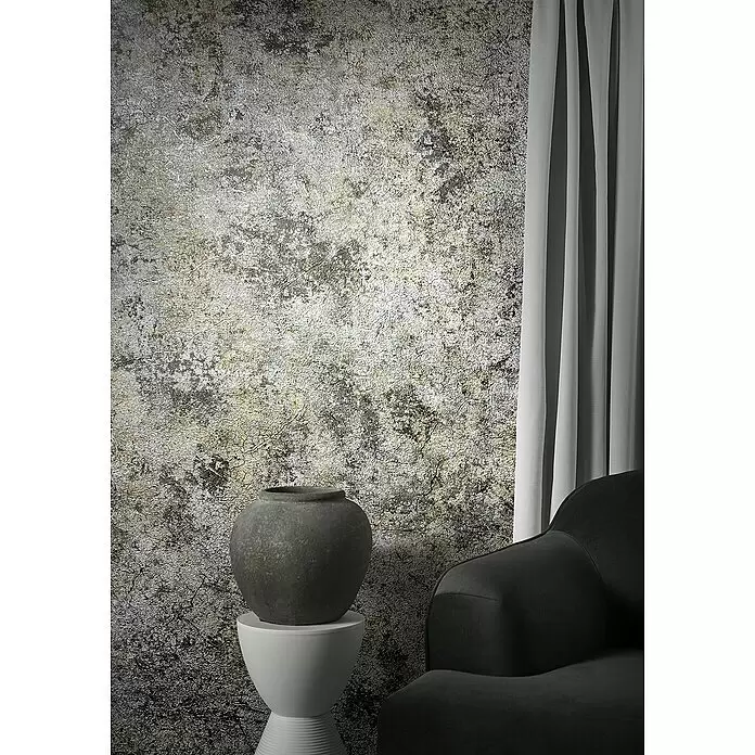 Marburg Natural Opulence Vliestapete Struktur I - Silber, Betonoptik, 10,05 x 0,7 m - Texturierte Metalltapete in Grau-, Gold- und Schwarztönen, neben einer dunklen Vase auf einem weißen Hocker und einem grauen Sessel.