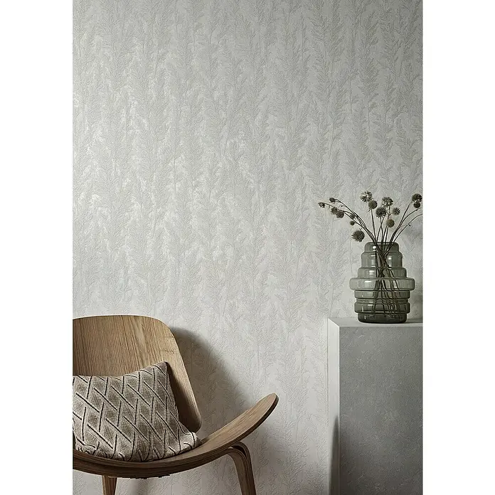 Marburg Natural Opulence Vliestapete Weiche Gräser - Grau, Floral, 10,05 x 0,7 m - Nahaufnahme eines Stuhls mit Kissen und Vase vor einer weißen Wand mit Blattmuster.