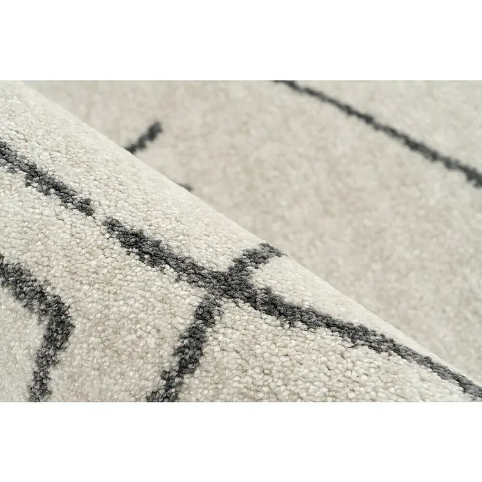 Kurzflorteppich Agadir - Ivory, 170 x 120 cm, 100% Polypropylen (Flor) - Detailaufnahme eines gerollten Teppichs mit hellem Grundton und modernem, geometrischem Muster in dunkler Farbe.