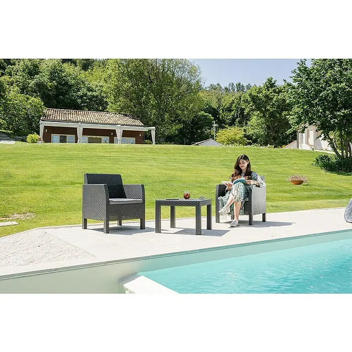 Toomax Loungemöbel-Set Matilde - Kunststoff, Schwarz, 3 -tlg. - Ein entspannendes Bild mit stilvollen Gartenmöbeln, darunter ein Sessel und ein Tisch, neben einem glitzernden Pool auf einer grünen Wiese.