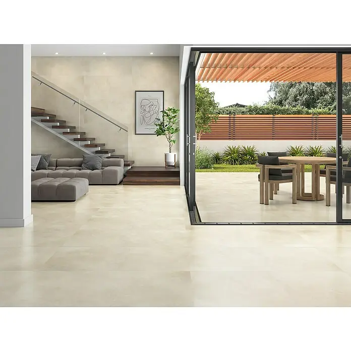 Halcón Pavimento porcelánico Energy - 120 x 60 cm, Ivory, Mate, Rectificado, Espesor: 9,5 mm - Elegante salón con baldosas beige, una escalera moderna y vistas a un patio con muebles de exterior a través de grandes puertas correderas.