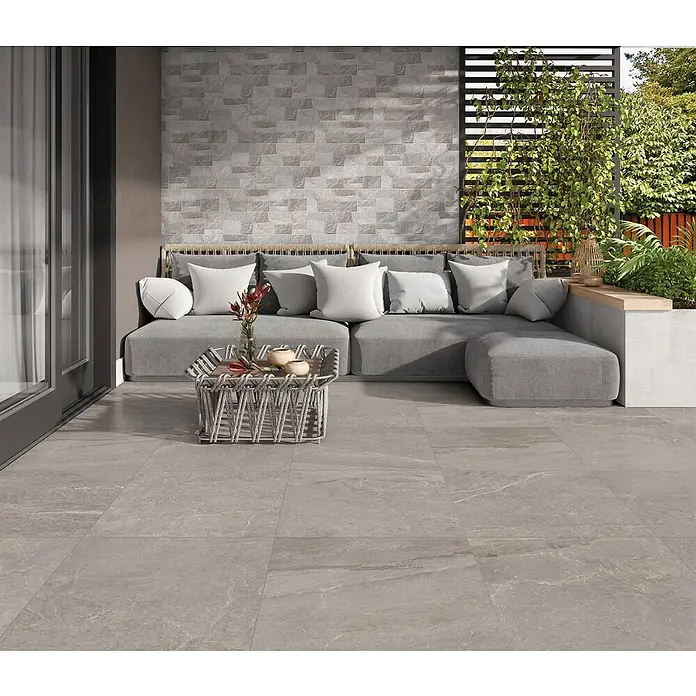 Halcón Pavimento porcelánico Tempo - 60,5 x 60,5 cm, Ash, Mate, Clase 3 Antideslizante - Baldosas grises en un patio con sofá y mesa de centro que crean un espacio exterior moderno y elegante. Las baldosas son duraderas y fáciles de mantener.
