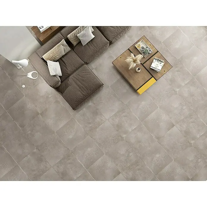 BHS Showroom Pavimento porcelánico Energy - 60,5 x 60,5 cm, Taupe, Mate - Vista superior de una sala de estar con baldosas grises, un sofá y una mesa de centro con objetos decorativos.