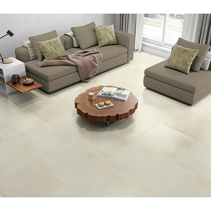 BHS Showroom Pavimento porcelánico Energy - 60,5 x 60,5 cm, Ivory, Mate - La imagen muestra un conjunto de sofás moderno con una mesa de madera adornada con elementos decorativos y revistas, sobre un fondo luminoso.