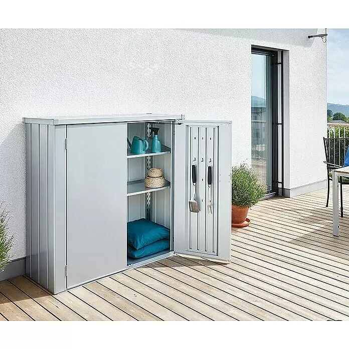 Biohort Romeo Geräteschrank Romeo Gr. M - Außenmaß inkl. Dachüberstand (B x T): 132 x 57 cm, Stahl, Silber-Metallic - Grauer Metall-Gartenschrank mit offenen Türen, Regalen, Gartenartikeln und Grillwerkzeugen auf einer Holzterrasse.