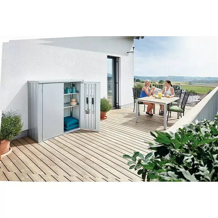 Biohort Romeo Geräteschrank Romeo Gr. M - Außenmaß inkl. Dachüberstand (B x T): 132 x 57 cm, Stahl, Silber-Metallic - Grauer Metall-Outdoor-Schrank mit offener Tür auf Holzterrasse, mit Kissen, Gießkannen und Grillwerkzeug.