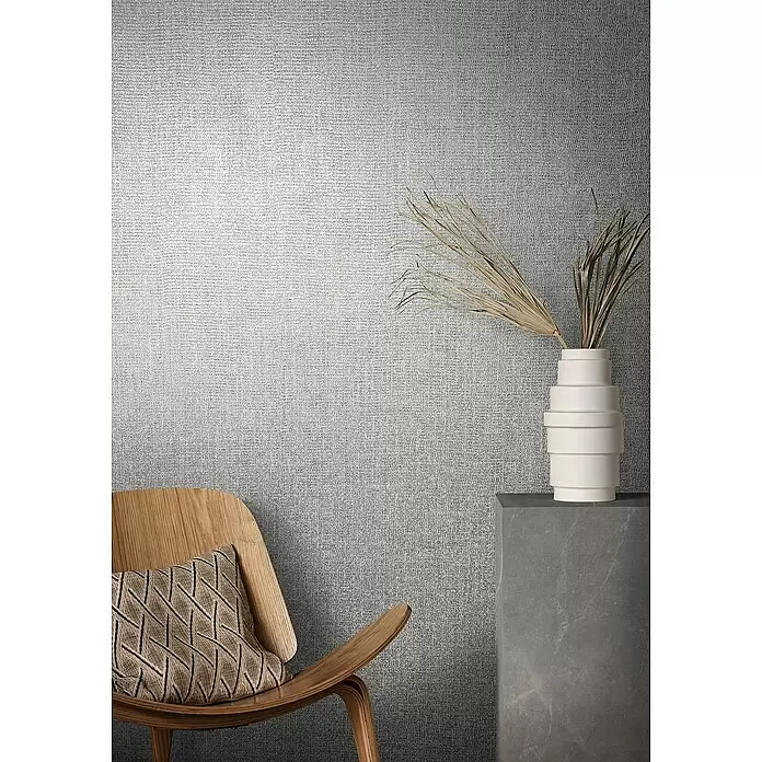Marburg Natural Opulence Vliestapete - Grau-Grün, Uni, 10,05 x 0,7 m - Texturierte hellgraue Wandverkleidung in Leinenoptik, die einen modernen Wohnraum hinter einem Holzstuhl und Beistelltisch aufwertet.