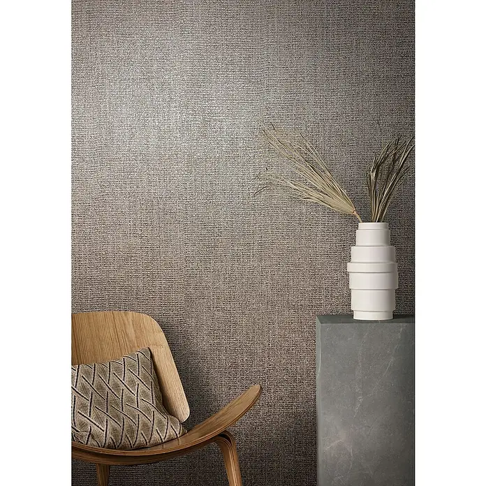 Marburg Natural Opulence Vliestapete - Rot-Braun, Uni, 10,05 x 0,7 m - Nahaufnahme eines Innenraums mit einer texturierten Tapete, einem Holzstuhl mit Kissen und einer Vase mit getrockneten Pflanzen auf einem grauen Sockel.