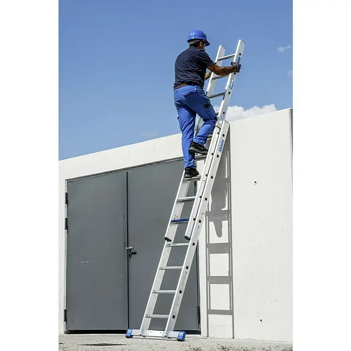 Krause Stabilo Schiebeleiter +S - Anzahl Tritte: 18 Stk., Arbeitshöhe: 5,15 m, Aluminium - Ein Bauarbeiter steigt mit einem blauen Helm auf eine ausziehbare, weisse Krause Leiter, die an einer weissen Wand lehnt.