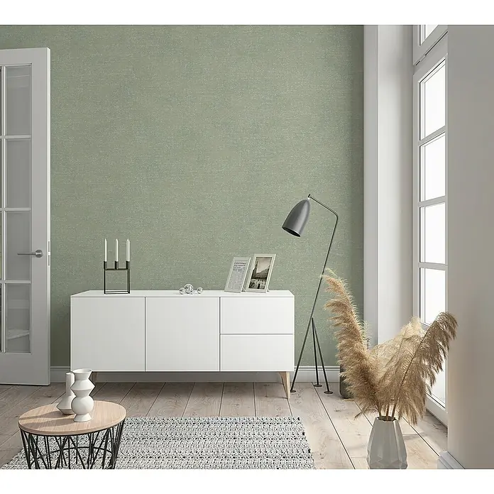 Marburg Shades Vliestapete - Grau-Beige, Uni, 10,05 x 0,53 m - Einrichtung mit weißem Sideboard, Stehlampe und minimalistischer Dekoration vor einer grünen Wand.