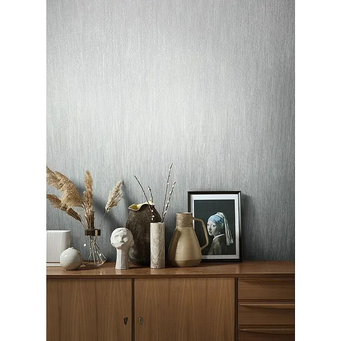 Marburg Natural Opulence Vliestapete - Grau, Streifen, 10,05 x 0,7 m - Wandbild mit Stillleben-Arrangement, das Vasen, eine Skulptur und ein gerahmtes Gemälde auf einem Holzschrank zeigt, vor einer strukturierten Tapete.