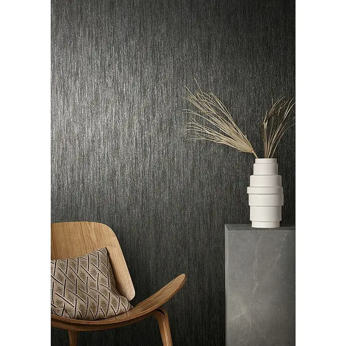Marburg Natural Opulence Vliestapete - Schwarz, Streifen, 10,05 x 0,7 m - Elegante Wandgestaltung mit einer schwarzen Tapete, die eine feine, vertikale Struktur aufweist. Ein heller Kontrast entsteht durch den Stuhl, das Kissen und die Dekoration.
