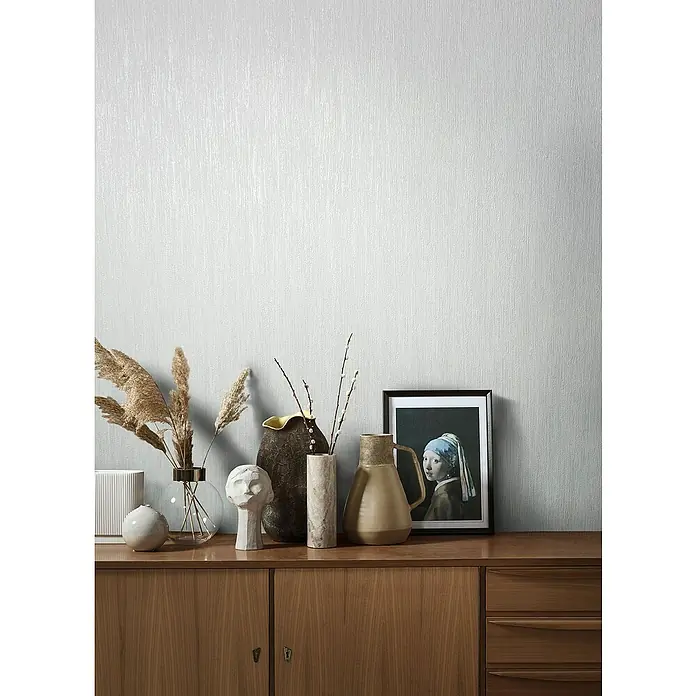 Marburg Natural Opulence Vliestapete - Metallic-Weiß, Streifen, 10,05 x 0,7 m - Eine Nahaufnahme einer Kommode mit diversen Dekorationsartikeln wie Vasen, einer Skulptur und einem gerahmten Bild der "Mädchen mit dem Perlenohrring".