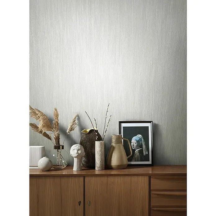 Marburg Natural Opulence Vliestapete - Weiß, Streifen, 10,05 x 0,7 m - Eine Nahaufnahme eines Sideboards mit verschiedenen Vasen und Deko-Objekten, sowie einem gerahmten Gemälde, alles auf einer Holzoberfläche.