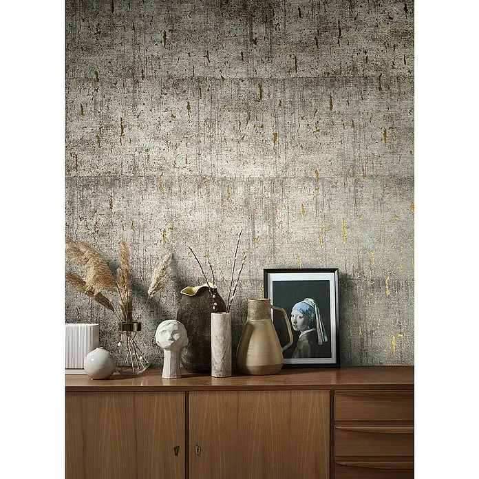 Marburg Natural Opulence Vliestapete - Greige, Betonoptik, 10,05 x 0,7 m - Stillleben mit Deko-Objekten auf einem Holzschrank vor einer grauen Wand mit goldenen Akzenten.