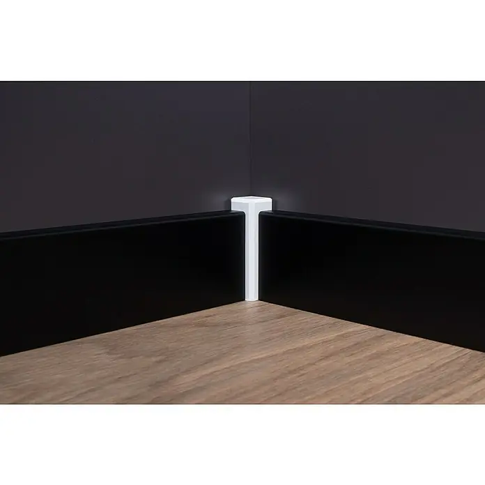 Sockelleiste - 240 cm x 16 mm x 58 mm, Fichte, Schwarz, Lackiert - Ecke einer Wand mit Fußleisten. Die schwarzen Fußleisten treffen sich an der weißen Eckleiste, die auf einem Holzboden steht.