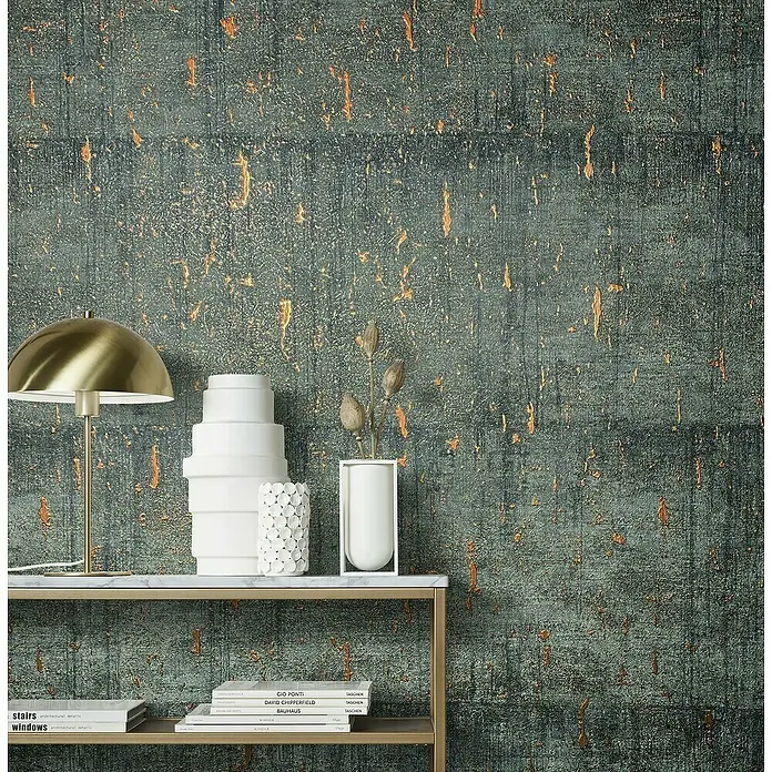 Marburg Natural Opulence Vliestapete - Anthrazit, Betonoptik, 10,05 x 0,7 m - Nahaufnahme eines Tisches mit Deko-Elementen und Büchern, vor einer strukturierten Wand. Elegante Einrichtung für modernes Wohnen.