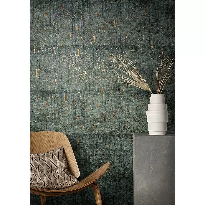 Marburg Natural Opulence Vliestapete - Anthrazit, Betonoptik, 10,05 x 0,7 m - Dunkeltürkise Tapete mit goldfarbenem Used-Look-Muster, die einen modernen Raum mit Stuhl und Vase akzentuiert.