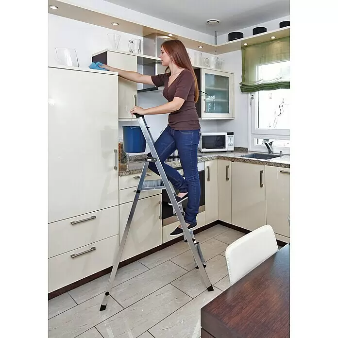Krause Monto Stehleiter Solidy - Arbeitshöhe: 3,25 m, Anzahl Tritte: 6 Stk., Belastbarkeit: 150 kg, Aluminium - Silberne Stehleiter, von einer Frau zum Reinigen hoher Küchenschränke verwendet.