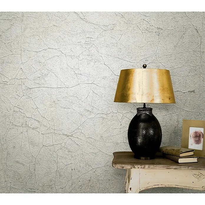 Marburg Vintage Deluxe Vliestapete Craquelée-Risse - Greige, Grafisch, 10,05 x 0,53 m - Dekorative Tischleuchte mit goldenem Schirm und verzierter Basis auf einem Beistelltisch, die ein warmes, einladendes Licht spendet.