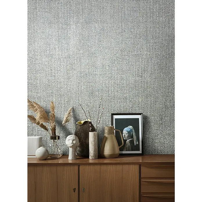 Marburg Natural Opulence Vliestapete - Grau-Silber, Uni, 10,05 x 0,7 m - Einrichtungsidee mit verschiedenen Vasen, Trockenblumen und einem Bild auf einem Holzschrank vor einer strukturierten Wandtapete.