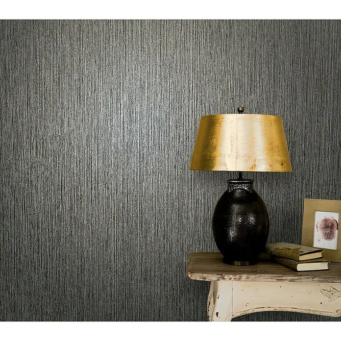 Marburg Vintage Deluxe Vliestapete - Anthrazit, Streifen, 10,05 x 0,53 m - Nahaufnahme eines Tisches mit Lampe, Büchern und einem Bilderrahmen vor einer strukturierten Tapete.